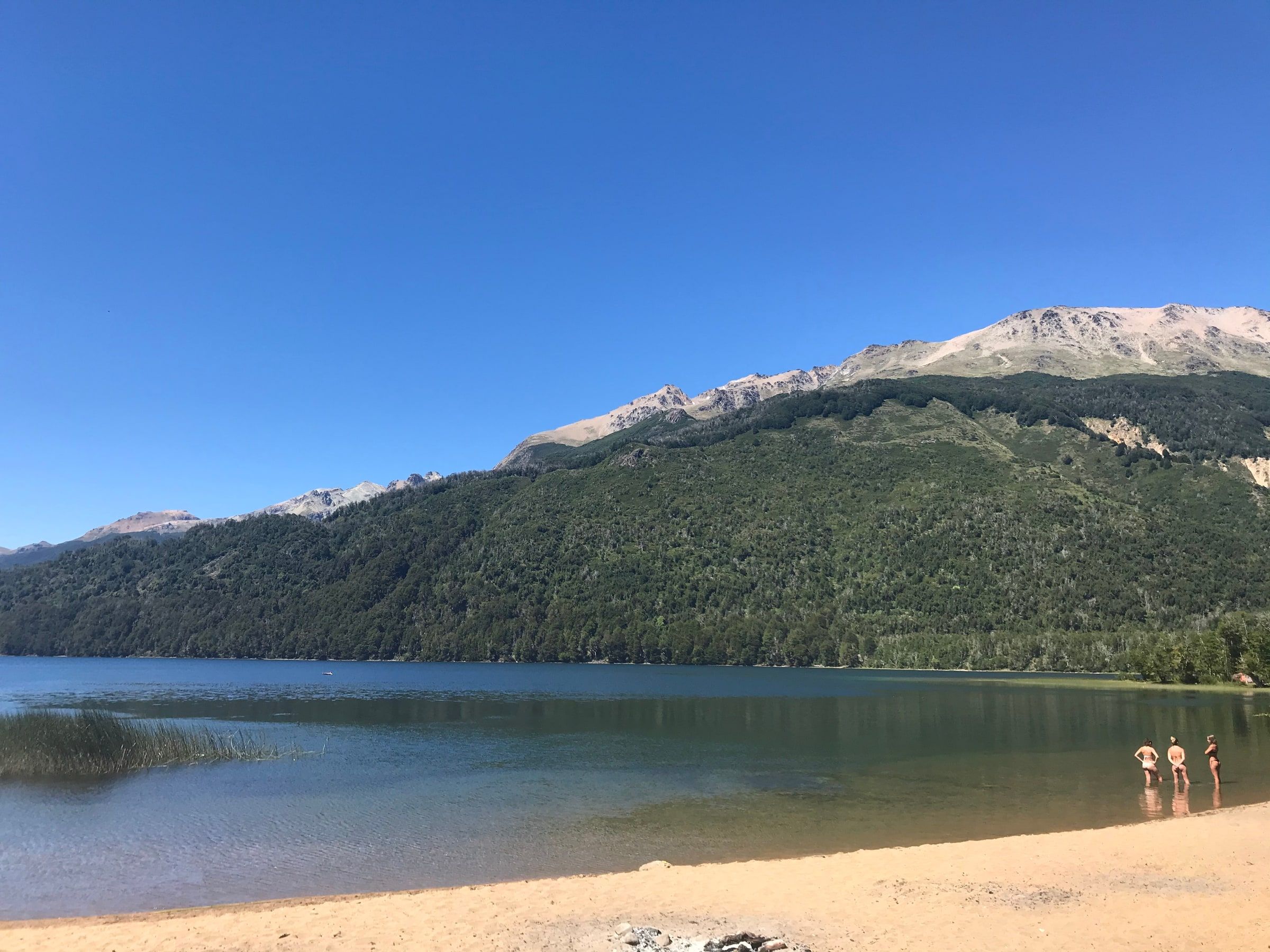 Un lago con playa de arena y montañas detrás
