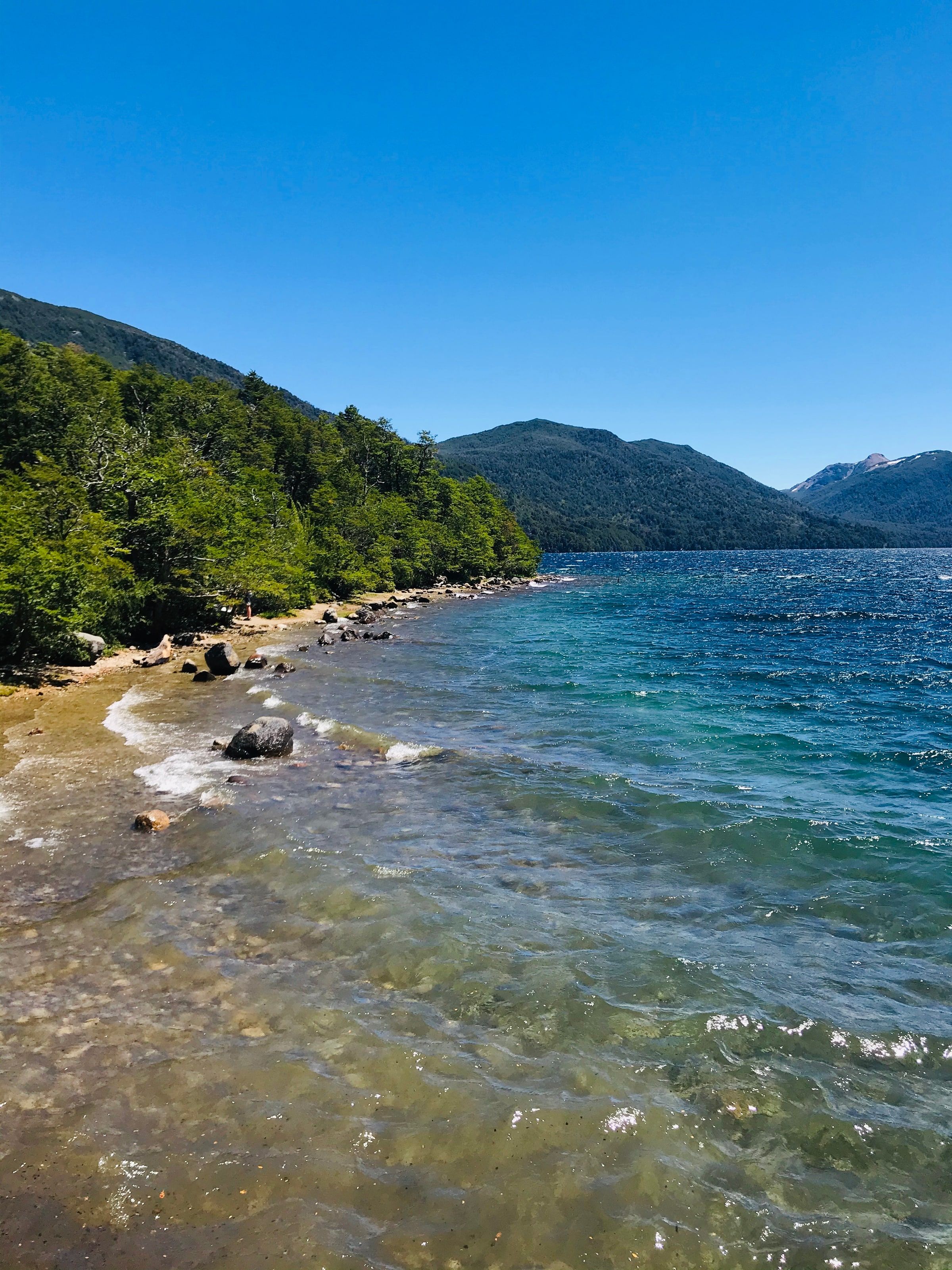Una playa de piedras con el agua transparente del lago