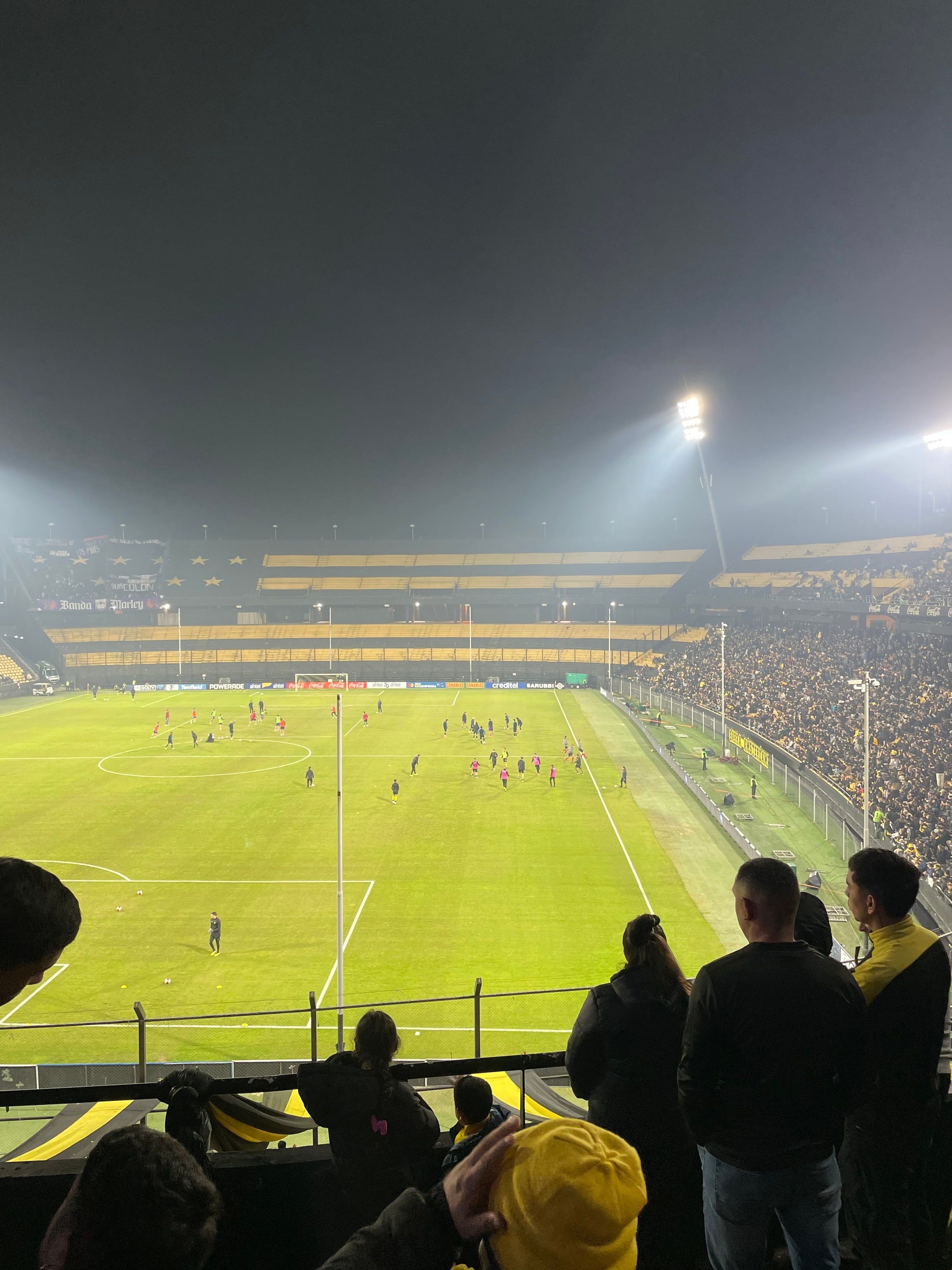 La cancha del Campeón del Siglo de noche, con niebla sobre las luces y el público de espaldas