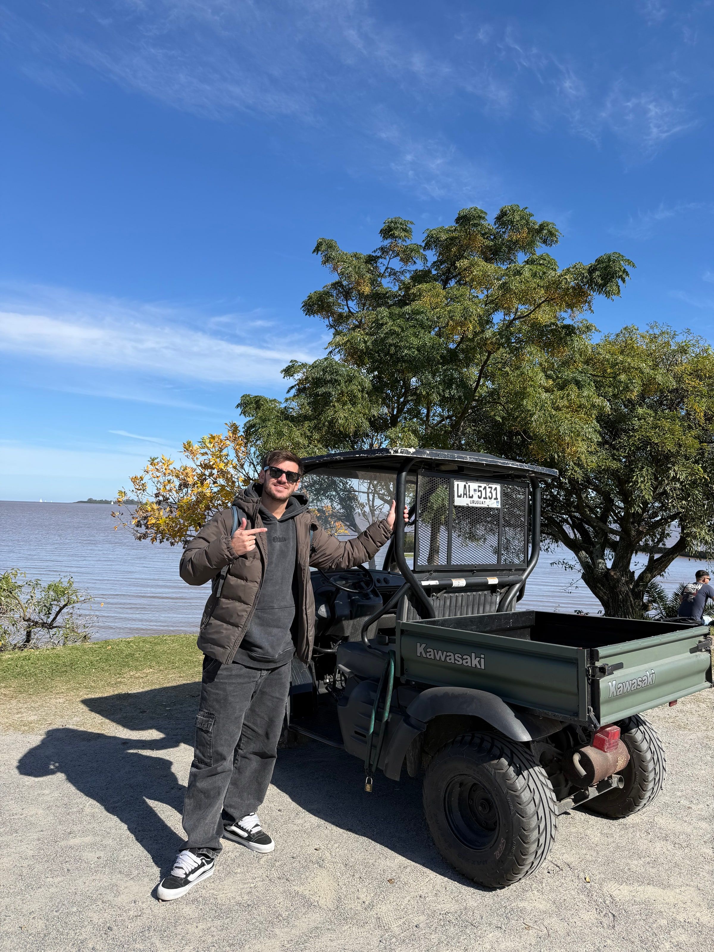 Tomi junto a un carrito de golf verde, con el río al fondo