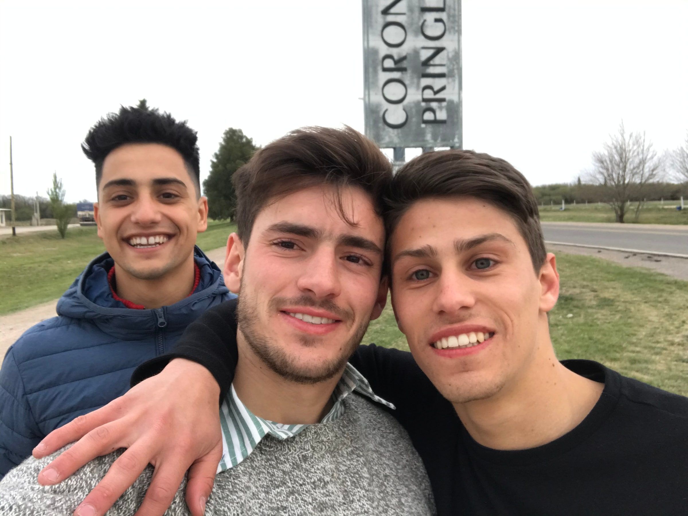 Selfie de tres amigos con el cartel de Coronel Pringles atrás