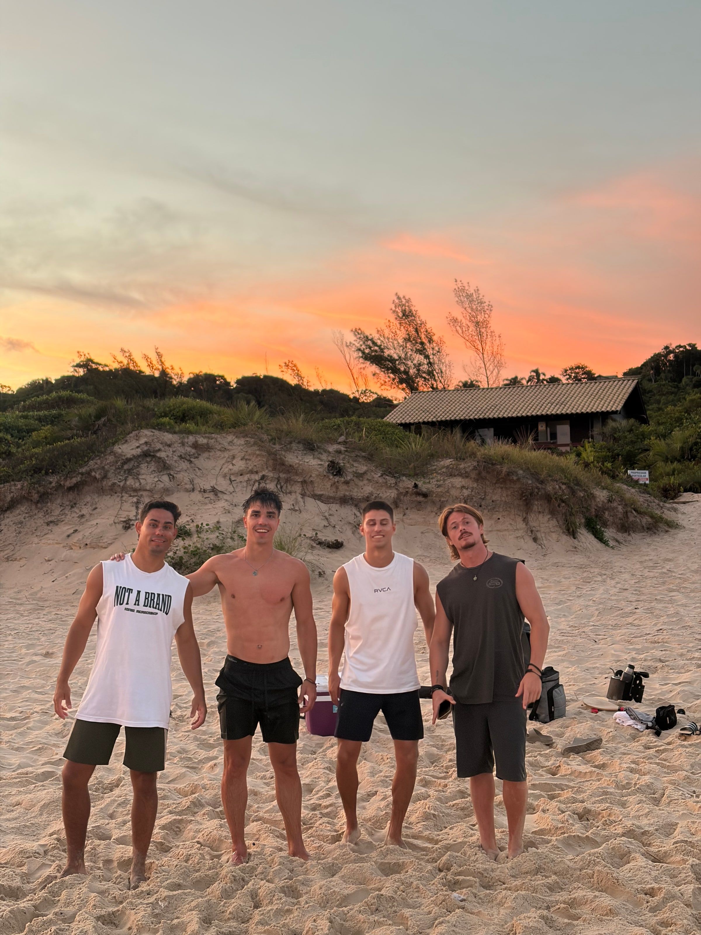 Cuatro amigos en la playa de Praia do Rosa con el atardecer naranja atrás