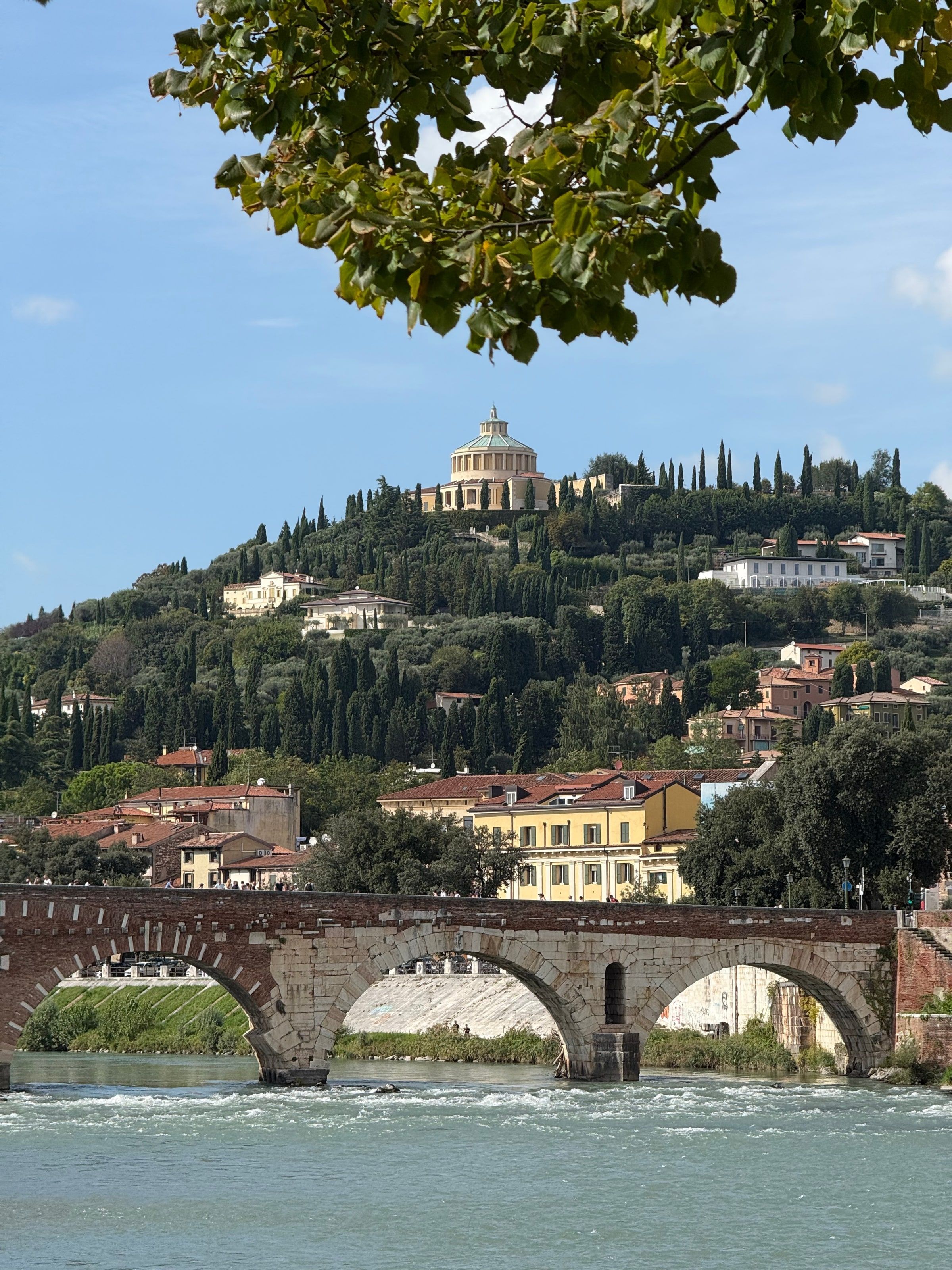 El Ponte Pietra sobre el Adige, con el santuario en la colina